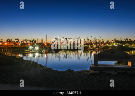 Cancella la riflessione di palme, barca a montanti e luci nelle calme acque dell'oceano di Ventura marina all'alba. Foto Stock