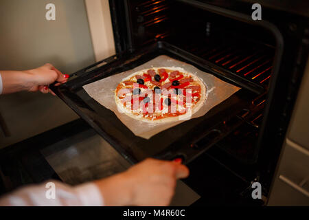 Donna mettere materie pizza con ingredienti e pomodoro, spezie, salsicce sul vassoio di cottura in forno Foto Stock