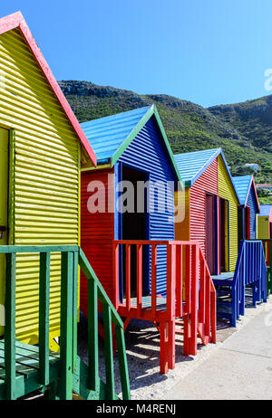 Famoso Vittoriano colorate scatole di balneazione presso San Giacomo Beach, Città del Capo, Sud Africa, presa su un soleggiato chiaro luminoso giorno sotto il cielo blu con le colline Foto Stock