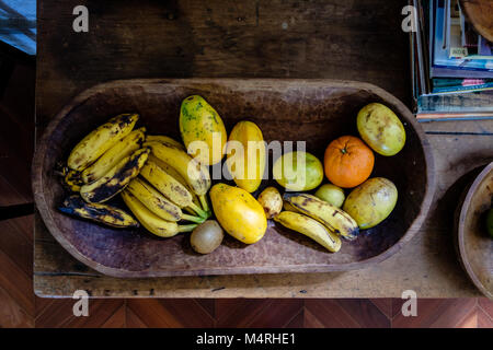 Vari frutti su un tagliere di legno con luce solare in arrivo. Ci sono delle banane, arance, papaya Foto Stock