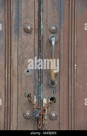 Un vecchio di legno per impieghi pesanti forte e sicuro porta o coppia di ante con un lucchetto e la catena mantenendolo al sicuro. maniglie e serrature delle porte su una grande porta resistente. Foto Stock