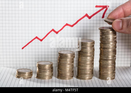 Una persona inserimento di moneta sulla moneta impilati con la freccia che mostra il profitto sul disegno quadrato sullo sfondo Foto Stock