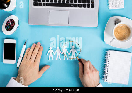 Close-up di un imprenditore che ingrandisce la carta tagliata fuori della figura umana sulla scrivania in ufficio Foto Stock