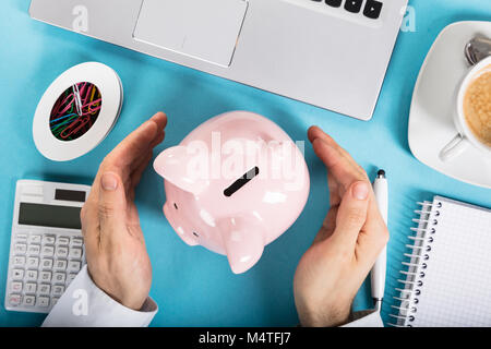 Vista in elevazione di un imprenditore proteggendo il Piggybank sulla scrivania in ufficio Foto Stock