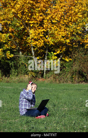 Bambina la riproduzione di laptop e ascoltare musica su cuffie nel parco Foto Stock