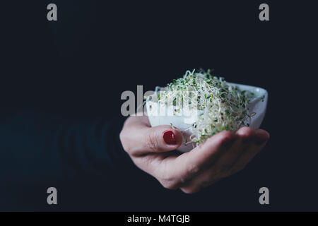 Donna contiene un mucchio di germogli alfalfa in una ciotola bianco Foto Stock