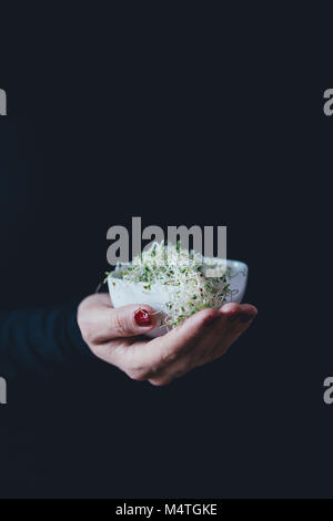 Donna contiene un mucchio di germogli alfalfa in una ciotola bianco Foto Stock