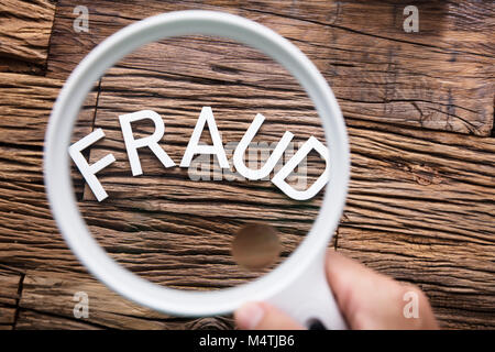 Una persona che guarda la frode bianco del testo tramite la lente di ingrandimento Foto Stock