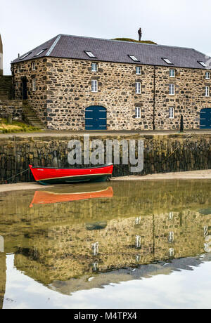 Rossa piccola barca a remi con la bassa marea, porto pittoresco, Dinnet, Aberdeenshire, Scozia, con acqua riflessioni e storico edificio Foto Stock