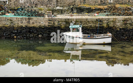 Piccola barca da pesca con la bassa marea, porto pittoresco, Dinnet, Aberdeenshire, Scozia, con acqua riflessioni e astice pentole su pier Foto Stock