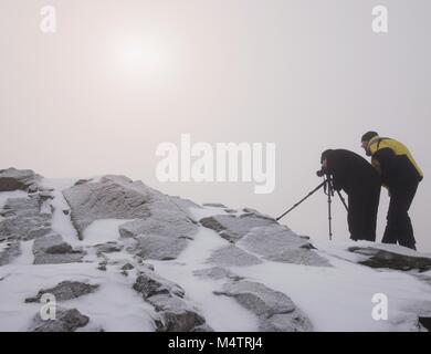 Gli escursionisti e appassionati di fotografia soggiorno sul picco innevato al treppiede. Gli uomini sulla scogliera di parlare e pensare. Inverno da sogno paesaggio con misty sunrise Foto Stock