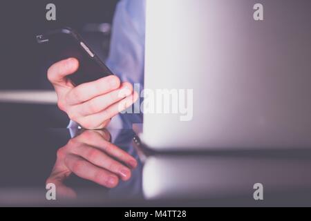 Ufficio caucasica lavoratore con lo smartphone e il computer portatile di fronte a lui. Il lavoro di ufficio tema. Foto Stock