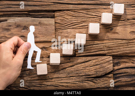 Close-up di Stepping a mano la carta tagliata fuori la figura sulla crescente blocchi disposti Foto Stock