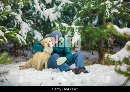 L'uomo abbracciando il Labrador retriever dog sitter in una foresta di pini in inverno Foto Stock