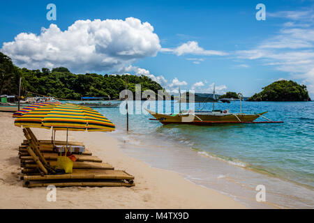 Bumboo lettini da sole con ombrelloni sulla sabbia, locale barca da pesca in acqua a Ilig Iligan Beach, Boracay Island, Filippine Foto Stock