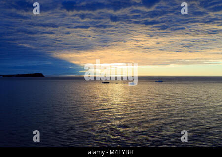 Tramonto nascosto da fitte nubi e riflessa in acqua di mare Foto Stock