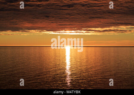 Tramonto nascosto da fitte nubi e riflessa in acqua di mare Foto Stock