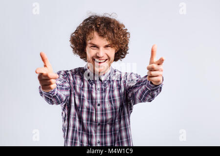 Un giovane curly-uomo dai capelli con un'emozione positiva punti proprio fing Foto Stock