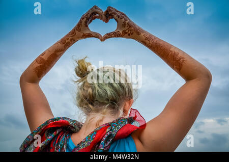 Bella ragazza bionda pone con henna dipinto le mani e le braccia sopra la sua testa a forma di cuore. Foto Stock