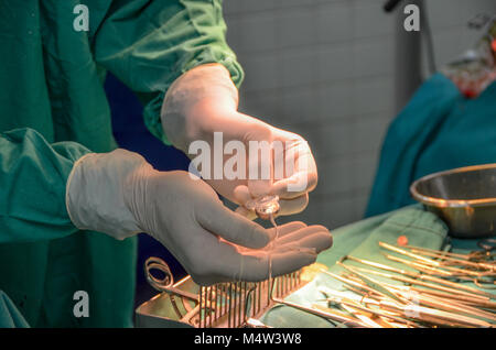 Un impianto cocleare tenutasi a guanto mani racchiuso da un chirurgo preparandosi per una operazione di impiantare un dispositivo auditivo. Foto Stock