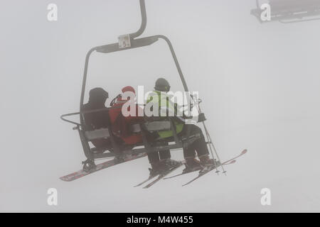 Tre persone montato su una seggiovia di un giorno di bufera di neve e nebbia in Sierra de Béjar ski resort - La Covatilla, Salamanca, Spagna. Foto Stock