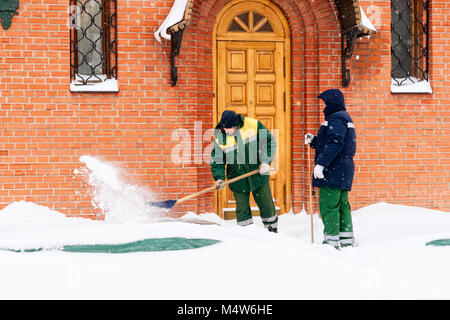 Mosca, 5 Febbraio 2018: Non identificato, irriconoscibile lavoratori con pale rimuovere la neve dall'ingresso all'edificio di mattoni rossi. Foto Stock