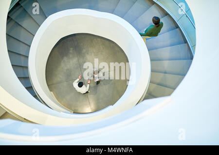 Ampio angolo di visione a due uomini di affari che stringono le mani in piedi al fondo della scala a chiocciola in ufficio moderno edificio, spazio di copia Foto Stock