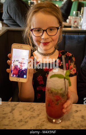 8 anno vecchia ragazza che mostra snapchat sul suo iPhone smart phone mentre seduto in un bar a bere un analcolico cocktail Foto Stock