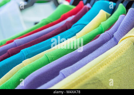 Il cotone magliette polo di vari colori blu giallo rosso viola verde bianco appeso su staffe sul rack in negozio di abbigliamento. Le vendite al dettaglio di moda consumismo Foto Stock