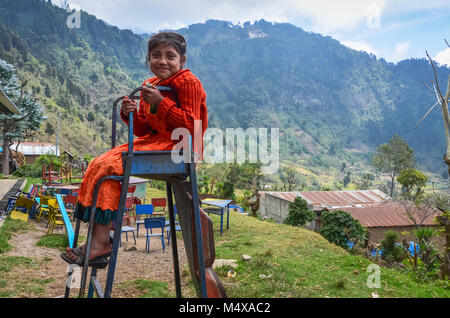 Sorridente giovane studente si siede in cima a una rotta in metallo scorrevole in corrispondenza di una zona rurale scuola guatemalteca dove tutti gli abitanti del villaggio vivono in povertà. Foto Stock