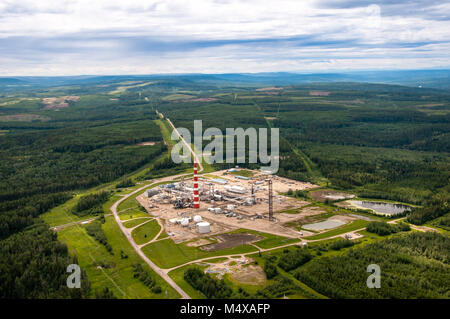 Impianto a gas ai piedi delle colline di Alberta in Canada. Montagne Rocciose in background. Il bianco e il rosso pile set contro il verde. Foto Stock