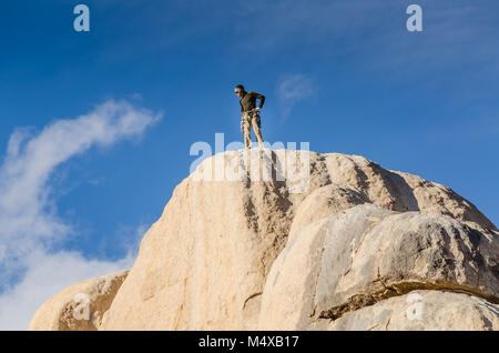 Un maschio di rocciatore sorge in cima al vertice di intersezione Rock, la prominente 150-piede alto monolito monzonite riconosciuto come il luogo di nascita di climbi Foto Stock