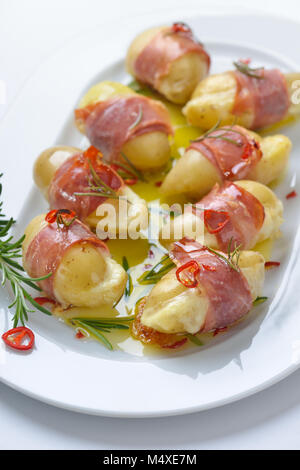 Hot rosmarino patate ripiene di formaggio e avvolto in Alto Adige, pancetta cotte in olio di oliva con fette di peperoncino Foto Stock