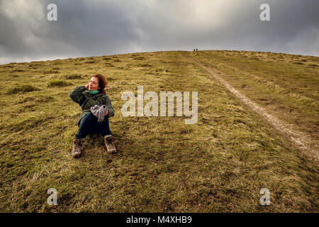 Un viandante si prende una pausa sulla collina Wolstonbury, parte del South Downs in East Sussex Foto Stock