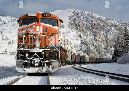 Un BNSF treno scendendo le tracce nella neve in un freddo, luminosa e soleggiata giornata. A Bearmouth, a ovest di Drummond, Montana nella contea di granito. Foto Stock