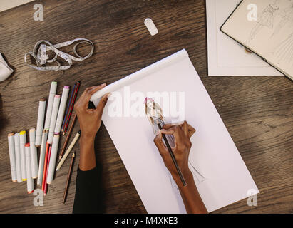 Vista superiore del designer di moda abbozzare un disegno seduto alla sua tavola. Ritagliato colpo di donna imprenditore lavorando su i suoi disegni alla sua scrivania. Foto Stock