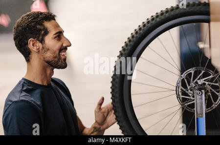 Uomo al lavoro su una bicicletta in un negozio di riparazione. Lavoratore allineamento di una ruota di bicicletta in officina. Foto Stock