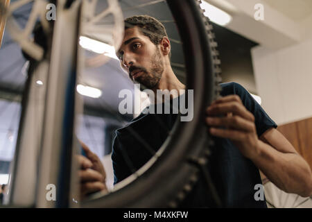 Lavoratore allineamento di una ruota di bicicletta in officina. Uomo al lavoro su una bicicletta in un negozio di riparazione. Foto Stock