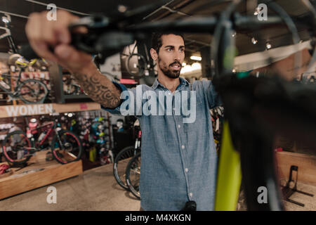 Uomo di ispezionare una maniglia di bicicletta per l'allineamento in una showroom. L uomo a una bicicletta showroom guardando le biciclette. Foto Stock