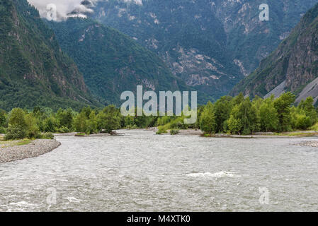 Un veloce fiume di montagna che scorre nella valle tra le montagne, con la foresta e le nuvole sulle piste da sci Foto Stock