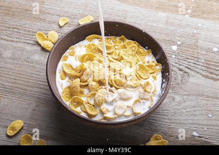 In un vaso di argilla con fiocchi di mais versando il latte. Piastra sorge su una superficie di legno. Foto Stock