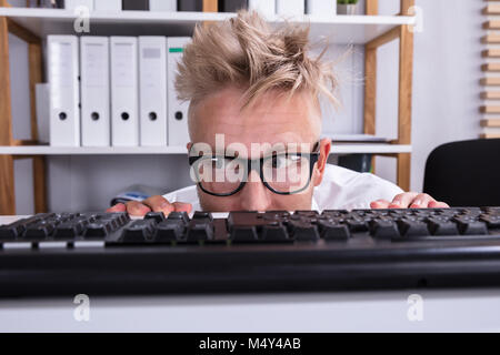 Imprenditore divertenti indossando occhiali nascondendo dietro la scrivania in ufficio Foto Stock