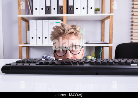 Imprenditore divertenti indossando occhiali nascondendo dietro la scrivania in ufficio Foto Stock