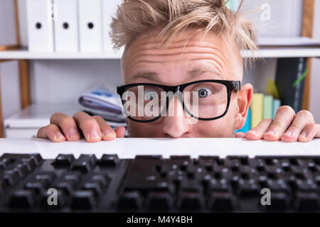 Imprenditore divertenti indossando occhiali nascondendo dietro la scrivania in ufficio Foto Stock