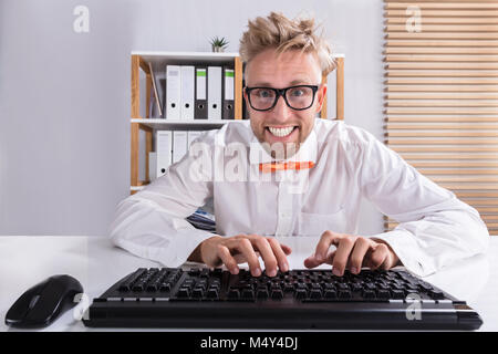 Sorridente giovane imprenditore in arancione Bow digitando sulla tastiera in ufficio Foto Stock