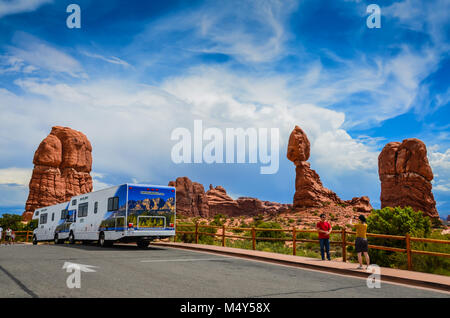 Turisti asiatici scattare fotografie di fronte equilibrato di Rock, mentre due RVs rimangono parcheggiate dalla meraviglia naturale. Parco nazionale Great Basin, Moab, UT Foto Stock