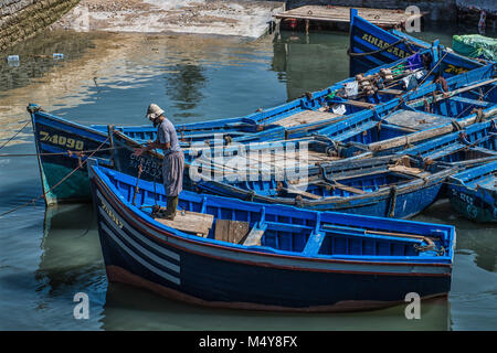 Un pescatore locale funziona sul blu iconico barche nel porto di pesca di Essaouira. Le barche e acqua sono un brillante colore blu. Foto Stock