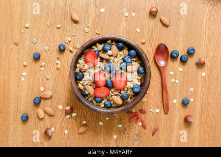 Ciotola di muesli con fragole fresche e mirtilli sul tavolo di legno. Lay piatto, il concetto di uno stile di vita sano, mangiare sano, dieta bilanciata e mea Foto Stock