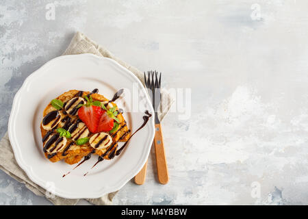 French Toast con lo sciroppo al cioccolato e fragole e una banana. Sfondo grigio, copia spazio, vista dall'alto. Foto Stock