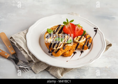 French Toast con lo sciroppo al cioccolato e fragole e una banana. Sfondo grigio, copia spazio, vista dall'alto. Foto Stock